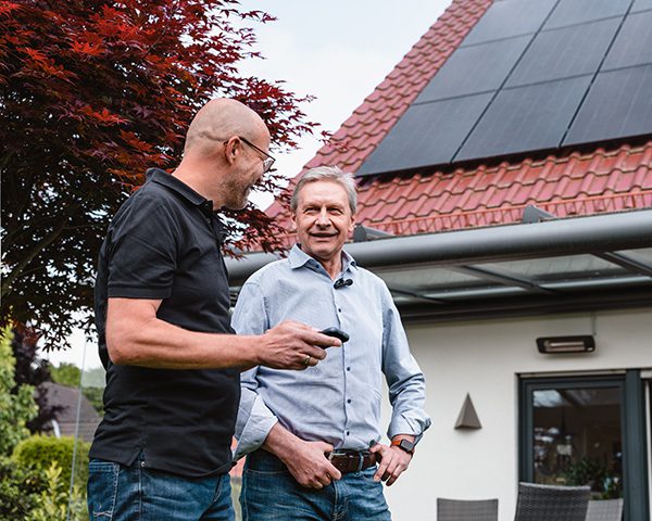 Ein enerix-Mitarbeiter berät einen Kunden im Garten vor einem Haus