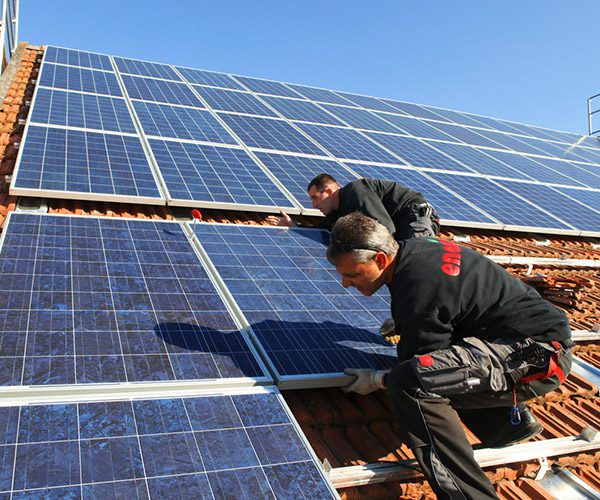 Handwerker montieren ein Solarmodul auf dem Hausdach eines Einfamilienhauses