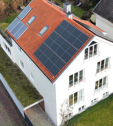 Ein Mehrfamilienhaus mit einer großen Photovoltaikanlage auf dem Dach, die zur nachhaltigen Energieversorgung beiträgt.